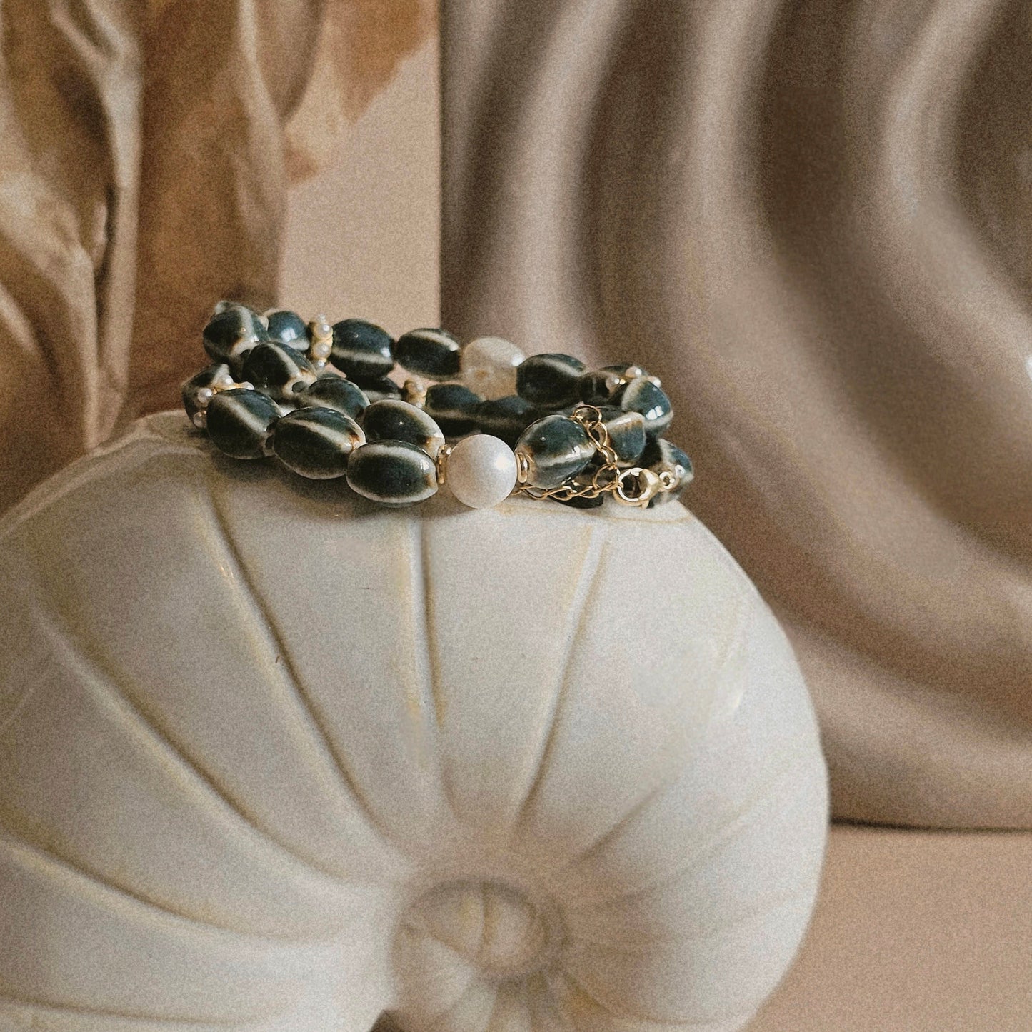 Bracelet with green stones and pearls on a shell against a beige fabric background
