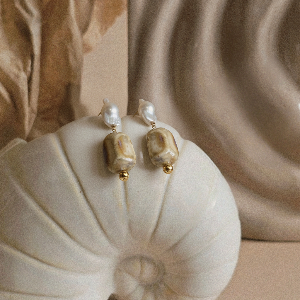 Pair of pearl earrings on a shell with a beige background