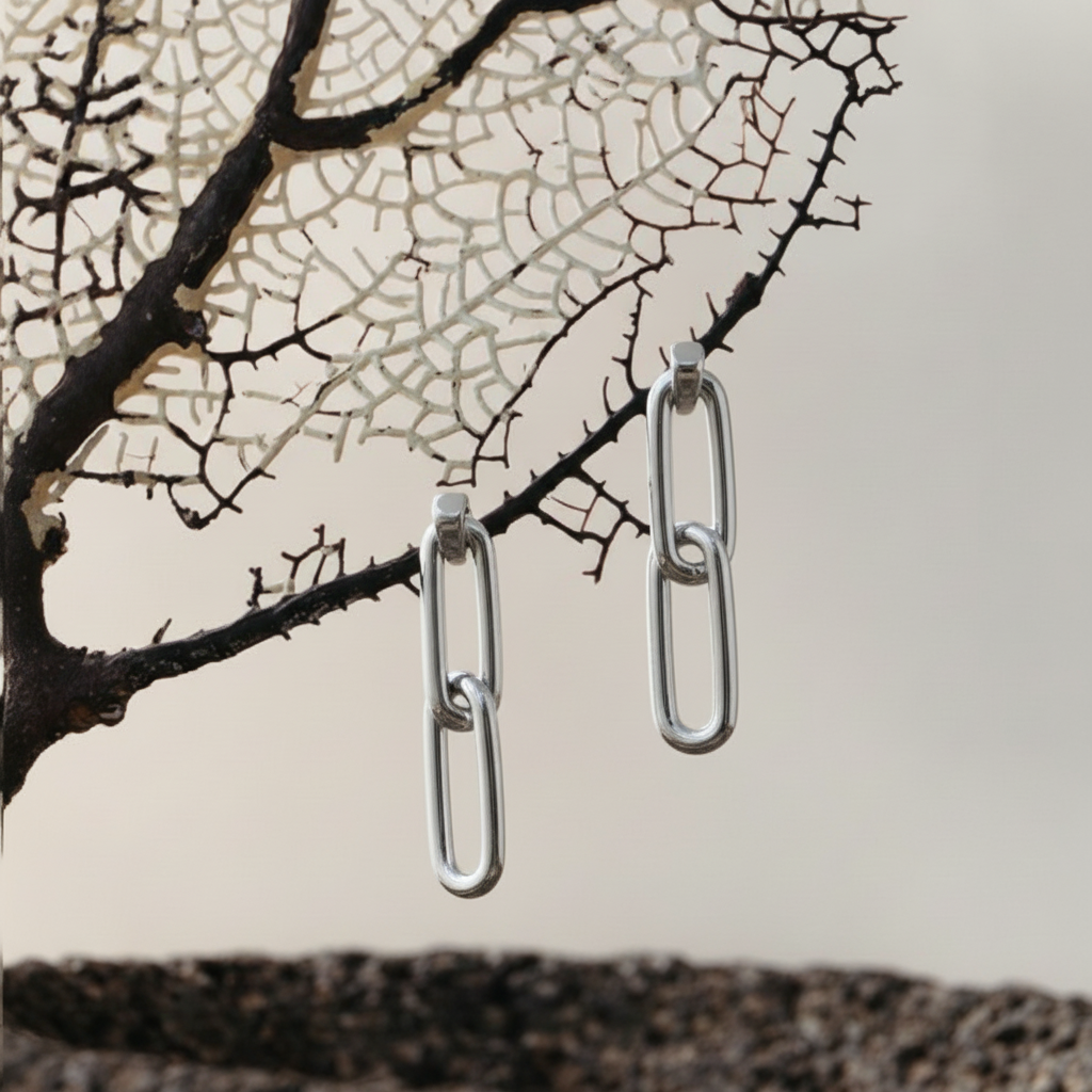 Silver chain-link earrings against a decorative background with tree branches.