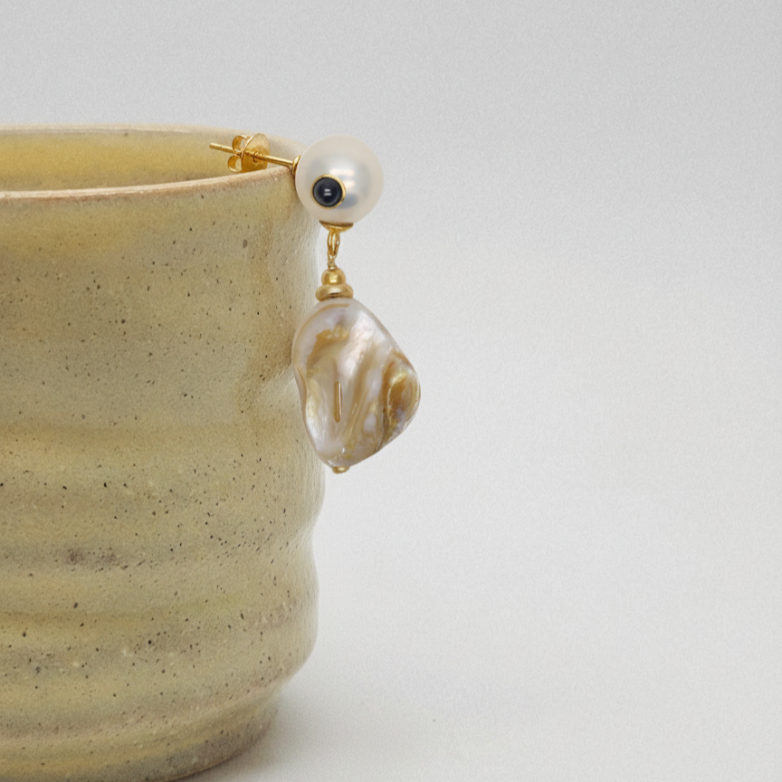Pearl earring with gold setting on a beige ceramic cup against a white background