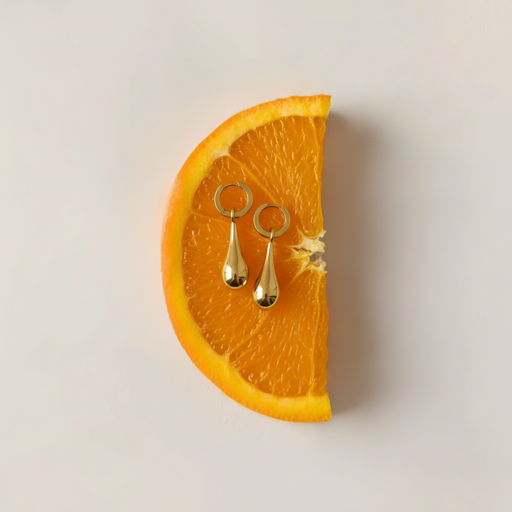 Gold earrings on a slice of orange against a light background