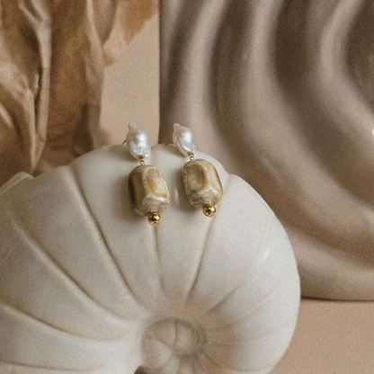 Pair of pearl earrings on a shell with a beige background