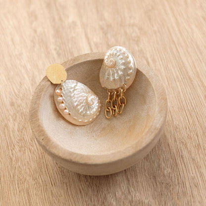 Pair of pearl and gold earrings on a wooden dish with a wooden background