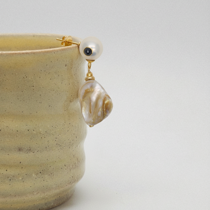 Pearl earring with gold setting on a beige ceramic cup against a white background