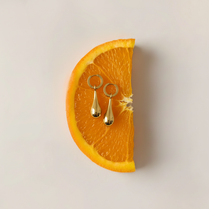 Gold earrings on a slice of orange against a light background